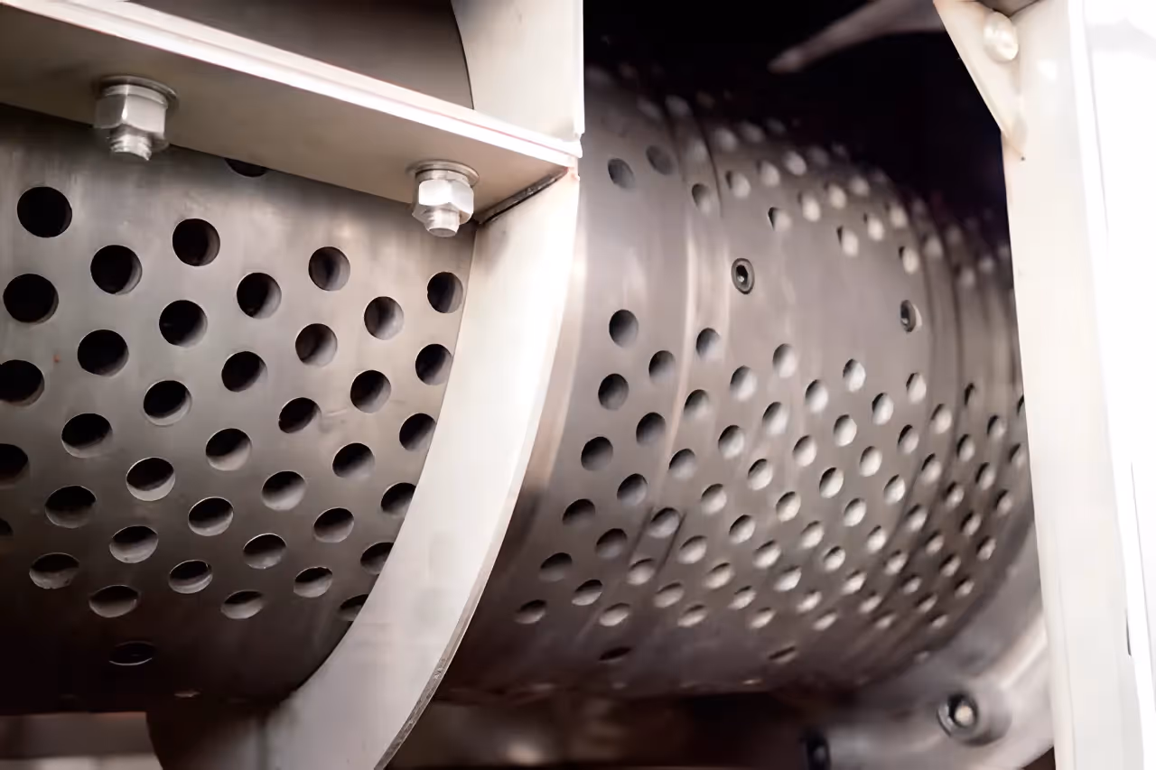 A close-up of the perforated stainless steel dewatering screen inside a plastic film squeezer, used for separating water from the film.
